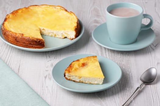 Delicious homemade cottage cheese casserole served with a warm cup of hot beverage on a wooden table.