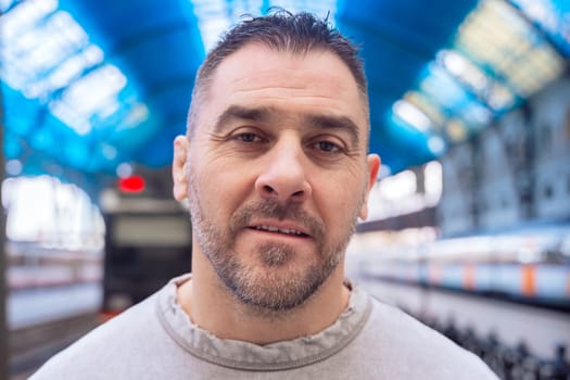 Close-up of a middle-aged man in a gray sweatshirt gazing upward at a train station. His contemplative expression conveys focus, waiting, and deep thought in an urban setting.