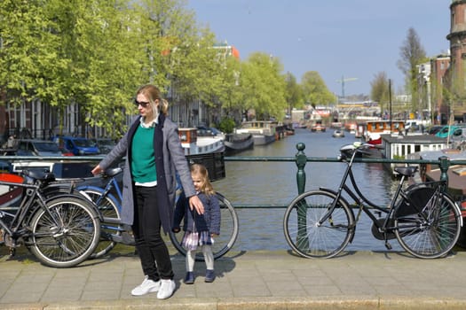 Blonde Dutchwoman mother with her daughter near the bicycle on the bridge over the water channel in Amsterdam city