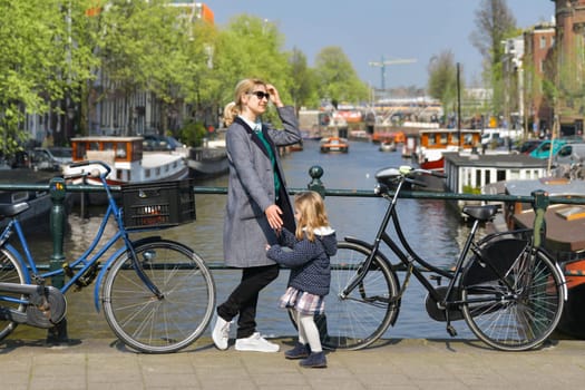 Blonde Dutchwoman mother with her daughter near the bicycle on the bridge over the water channel in Amsterdam city