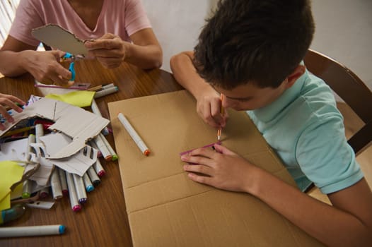 A young boy actively engages in a creative cardboard crafting project with adult guidance.