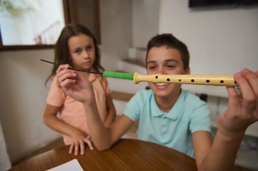 Two kids indoors examining a musical recorder, evoking curiosity about exploring music and learning.