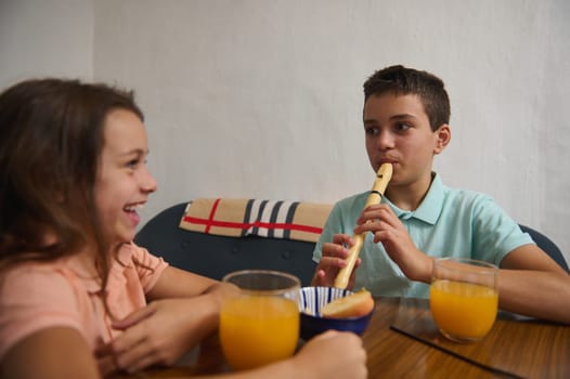 A boy plays a flute while a cheerful girl listens amusedly. They sit together, enjoying fruit juice in a warm and cozy setting, illustrating friendly interaction and joyful harmony.