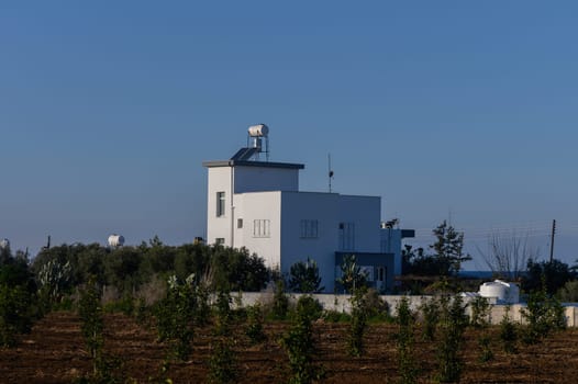 A modern white building is surrounded by lush greenery under a bright sky, showcasing serene rural beauty.