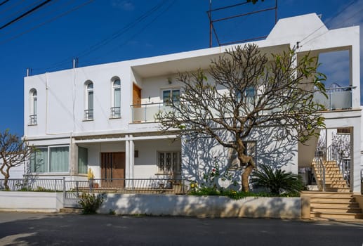 A beautiful white building stands under a clear blue sky, amid lush greenery and serene surroundings.