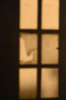 Golden light streams through a rustic window, creating delicate shadows that dance on the wall in a serene atmosphere.