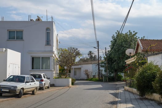 A tranquil residential area features white houses, green trees, and parked cars under a sunny blue sky.