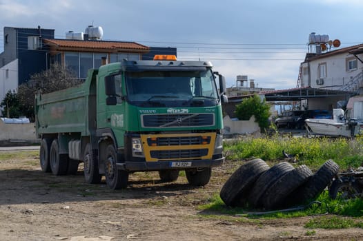 Gaziveren Cyprus -03.02.2025 A robust green truck stands idle in a rural area, surrounded by discarded tires beneath a clear sky.