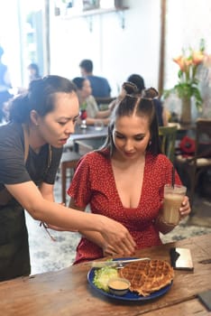 Vietnamese waitress served waffles to a Caucasian woman