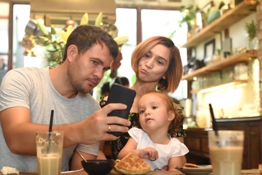 Young parents with daughter make selfie in a cafe
