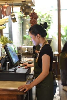 Young Vietnamese waitress working with check out machine