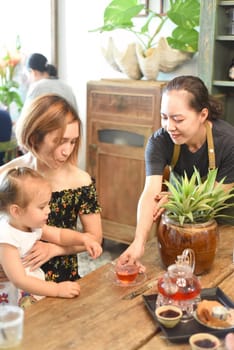 Vietnamese waitress serves hot tea for mother with daughter in cafe