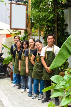 Vietnamese coffee shop team smiling and standing together against a cafe