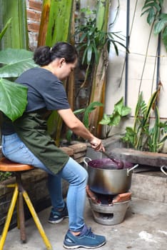 Young Vietnamese woman cooking a mulberry jam in a big saucepan