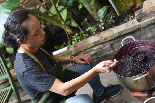 Young Vietnamese woman cooking a mulberry jam in a big saucepan