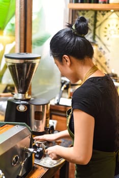 Vietnamese waitress making coffee via portafilter of a coffee machine