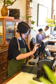 Young Vietnamese waitress serving a customer at the checkout in cafe.