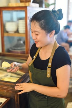 Vietnamese waitress showing a scoop of homemade mango ice cream in cafe