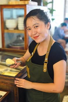 Vietnamese waitress showing a scoop of homemade mango ice cream in cafe