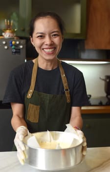 Vietnamese woman holding a baking dish with cheesecake dough in the kitchen