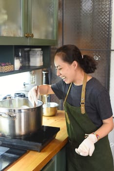 Young Vietnamese woman stirring  dough in a big metal saucepan