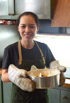 Vietnamese woman holding a baking dish with cheesecake dough in the kitchen