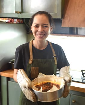 Vietnamese woman holding a baking dish with cheesecake dough in the kitchen