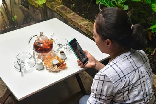 A woman taking picture of a glass teapot on a white table