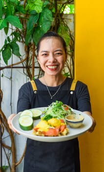 Young vietnamese waitress holding a plate with eggs bennedict waffles with smoked salmon in restaurant