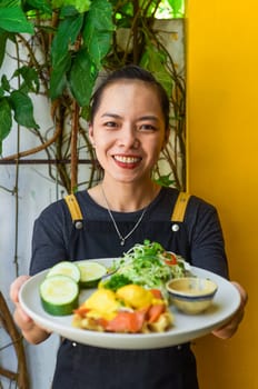 Young vietnamese waitress holding a plate with eggs bennedict waffles with smoked salmon in restaurant