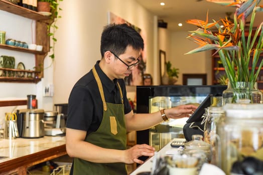 Vietnamese waiter working in counter with cashier machine in a cafe