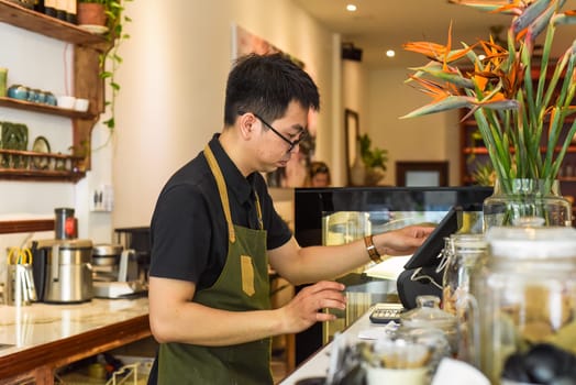 Vietnamese waiter working in counter with cashier machine in a cafe