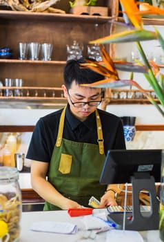 Vietnamese waiter working in counter with cashier machine in a cafe