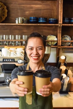 Vietnamese smiling waitress holding paper cups with coffee in a cafe