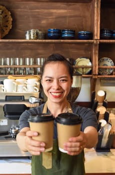 Vietnamese smiling waitress holding paper cups with coffee in a cafe
