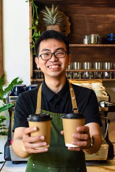 Vietnamese smiling waiter holding paper cups with coffee in a cafe