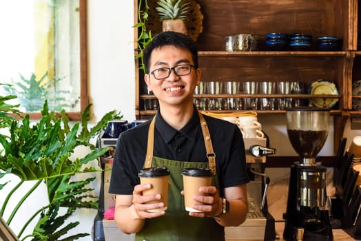 Vietnamese smiling waiter holding paper cups with coffee in a cafe