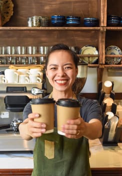 Vietnamese smiling waitress holding paper cups with coffee in a cafe