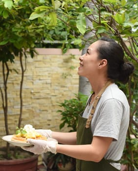 Vietnamese woman waitress serving Belgian waffles with fruits and ice cream in outdoor cafe looking up