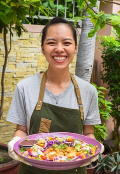Vietnamese woman waitress serving pan fried chicken with vegetables in outdoor cafe