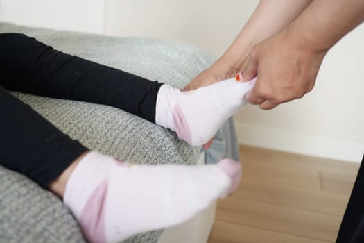 An adult assists a child in wearing pink socks in a cozy bedroom.