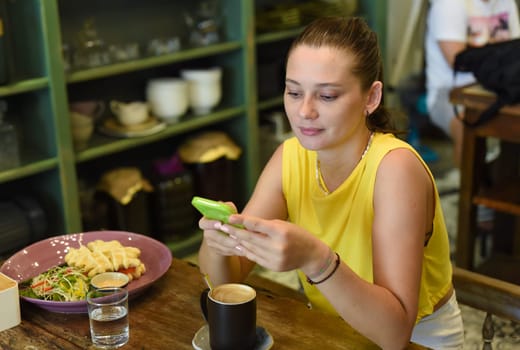 One caucasian woman scrolling a phone and preparing to eat her breakfast in cafe