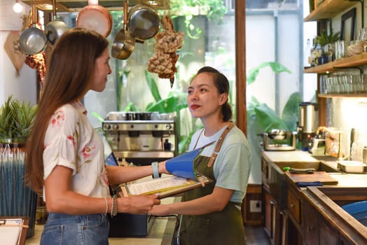 Young Vietnamese waitress working with check out machine and customers in cafe