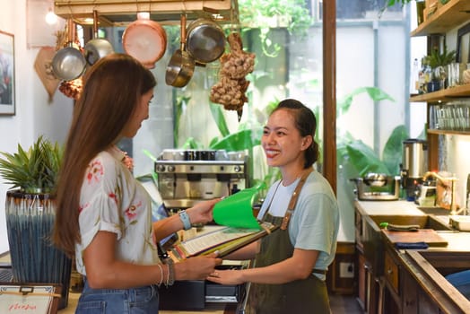 Young Vietnamese waitress working with check out machine and customers in cafe