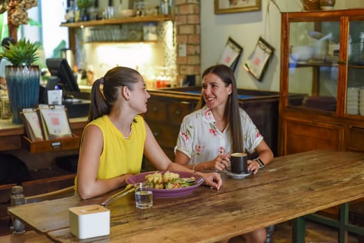 Two best friends talking and eating in a cafe