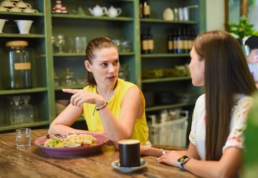 Two best friends talking and eating in a cafe