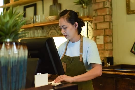 Young Vietnamese waitress working with check out machine in cafe