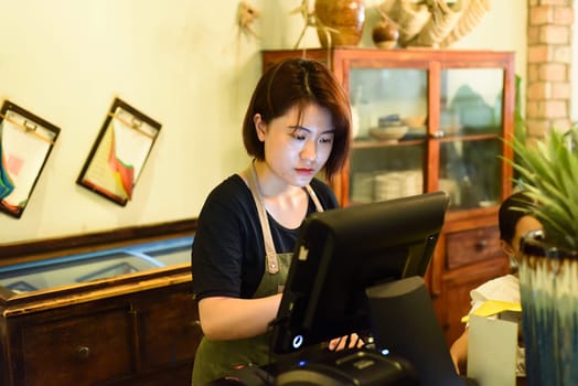 Young Vietnamese waitress working with check out machine in cafe