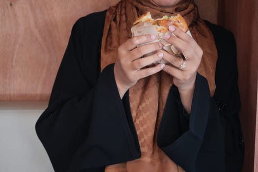 A woman clad in traditional clothing enjoys a hearty sandwich indoors.