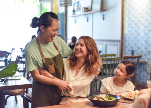 Little girl and her mother eating lunch and meeting their vietnamese friend waitress in a cafe